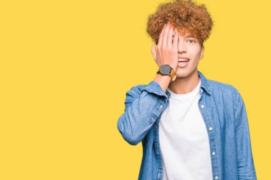 Afro saçlı Kot ceket kapsayan tek gözüyle el emin gülümseme ile yüz ve sürpriz duygu üzerinde giyen genç yakışıklı adam.