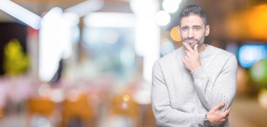 Emin çapraz kollar ve çeneme kaldırdı el ile gülümseme ile kameraya bakarak izole arka plan üzerinde kazak giyen genç yakışıklı adam. Pozitif düşünce.