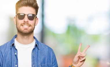 Mutlu yüz zafer işareti yaparken kameraya göz kırpıyor ile gülümseyen denim ceket giyen genç yakışıklı zarif adam. İki numaralı.