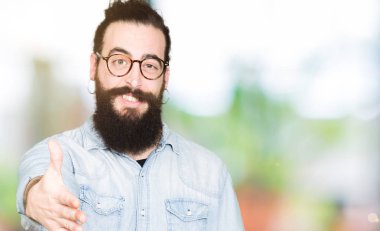 Uzun saç ve sakal tebrik ve konuksever dost sunan karşılıklı gülümseyen gözlüklü genç hipster adam. Başarılı iş.