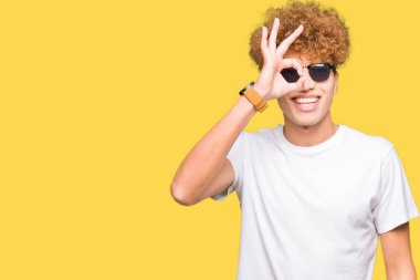 Gülümseyen, parmakları ile mutlu yüz üzerinden seyir göz el ile ok jest yapıyor güneş gözlüğü takıyor afro saçlı Genç yakışıklı adam.