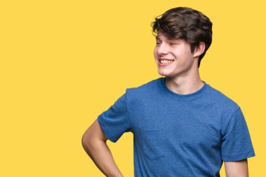 Uzak tarafına yüzünde, doğal ifade gülümseme ile seyir izole arka plan üzerinde mavi t-shirt giyen genç yakışıklı adam. Kendine güvenen gülüyor.