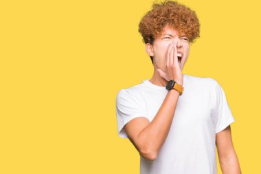 Afro saç ile genç yakışıklı adam rahat beyaz t-shirt bağırıyor ve ağzına el ile yan gürültülü çığlık giyiyor. İletişim konsepti.