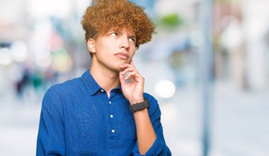 Çene düşünme hakkında soru, dalgın ifade üzerine el ile afro saçlı Genç yakışıklı zarif adam. Düşünceli yüzüyle gülümsüyor. Şüphe kavramı.