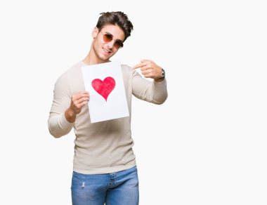 Kart kırmızı kalp ile izole arka plan üzerinde çok mutlu el ve parmak ile işaret tutan genç yakışıklı adam