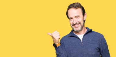 Orta yaş yakışıklı adam mutlu yüz görünümlü ve başparmak yukarı ile yan işaret ile gülümseyen bir kazak giyiyor.