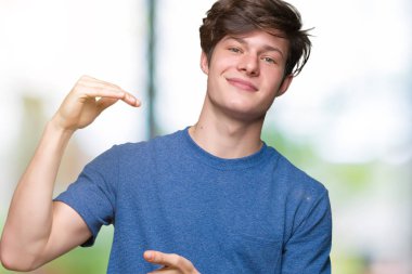 Genç yakışıklı adam ile büyük ve büyük boy işaret, ölçü birimi sembol gösteren el eller izole arka plan üzerinde mavi tişört giyiyor. Kameraya bakarak gülümsüyordu. Ölçüm kavramı.