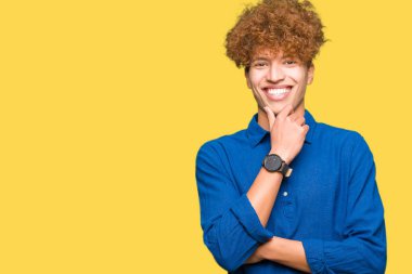 Afro saçlı Genç yakışıklı zarif adam çapraz silah ve el çene üzerinde yükseltilmiş ile gülümseme ile kamera emin görünümlü. Pozitif düşünme.