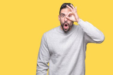 Sürpriz yüz, göz parmaklarının arasından seyir ile ok jest yapıyor izole arka plan üzerinde sweatshirt giyen genç yakışıklı adam şok. İmansız ifade.