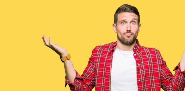 Yakışıklı adam rahat gömlek clueless ve şaşkın bir ifadeyle kollar ve eller kaldırdı giyiyor. Şüphe kavramı.