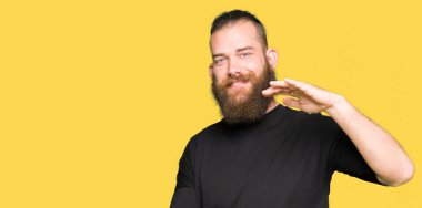 Büyük ve büyük boy işaret, ölçü birimi sembol gösteren elleriyle işaret rahat t-shirt giyen genç sarışın adam. Kameraya bakarak gülümsüyordu. Ölçüm kavramı.