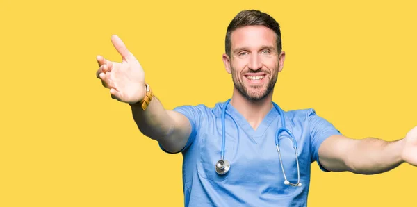 英俊的医生男子穿着医疗制服在孤立的背景看着镜头微笑着张开双臂拥抱 拥抱幸福的快乐表情 — 图库照片