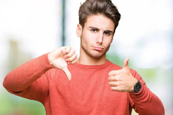 Young handsome man over isolated background Doing thumbs up and down, disagreement and agreement expression. Crazy conflict