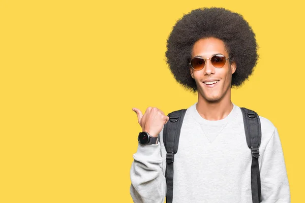非洲青年美国男子戴着太阳镜和背包 用大拇指指着和快乐的脸微笑着向一边展示 — 图库照片