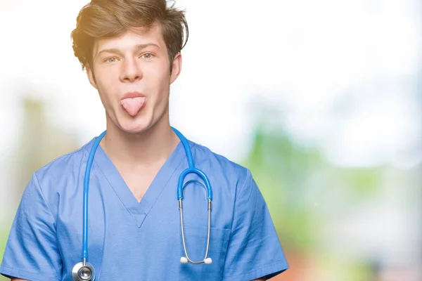 Joven Médico Vistiendo Uniforme Médico Sobre Fondo Aislado Sacando Lengua —  Fotos de Stock