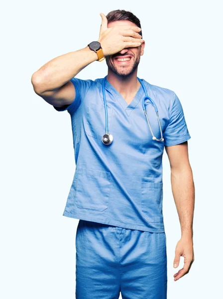 英俊的医生穿着医疗制服在孤立的背景微笑和笑着用手捂住眼睛惊喜 盲目的概念 — 图库照片