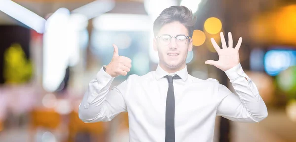 若いビジネス人にメガネをかけて分離を示す背景と自信を持って 幸せな笑みを浮かべて 指で上向きナンバーシックス — ストック写真