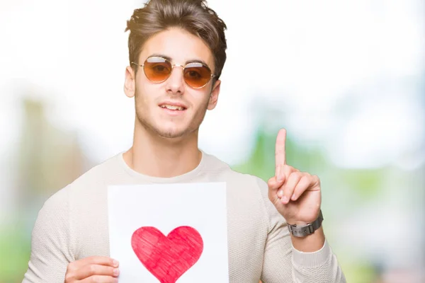 Joven Hombre Guapo Sosteniendo Tarjeta Con Corazón Rojo Sobre Fondo — Foto de Stock