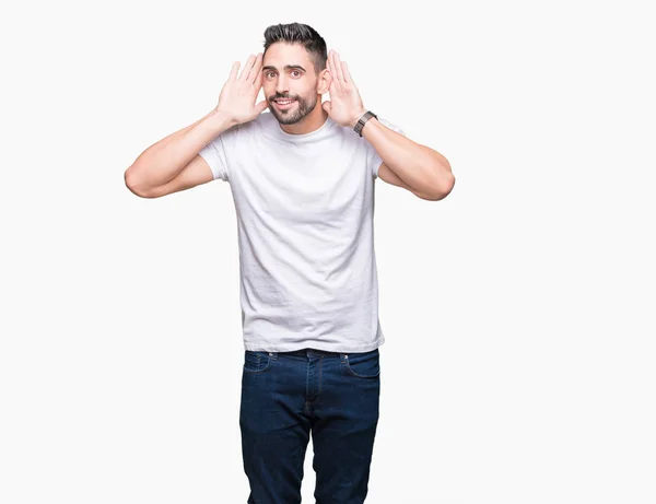 英俊的男子穿着白色T恤在白色孤立的背景试图听到双手的耳朵手势 好奇的八卦 听力问题 — 图库照片