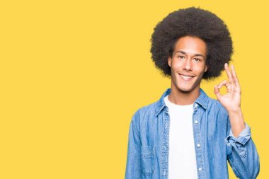 Afro saç gülümseyen genç Afro-Amerikan adam el ve parmaklar ok işaretiyle yapıyor olumlu. Başarılı ifade.