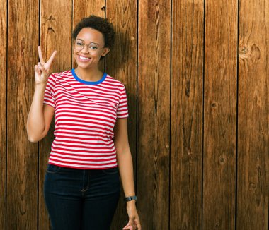 Güzel genç Afro-Amerikan kadın gözlük gösterilen ve parmakları ile işaret izole arka plan üzerinde kendinden emin ve mutlu gülümseyerek iken ikincisi.