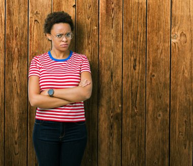 İzole arka plan şüpheci ve çapraz kolları olan yüzündeki gergin, onaylamayan ifade gözlüklü güzel genç Afro-Amerikan kadın. Negatif kişi.