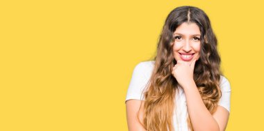 Emin çapraz kollar ve çeneme kaldırdı el ile gülümseme ile kameraya bakarak casual beyaz t-shirt giyen genç güzel kadın. Pozitif düşünce.