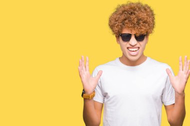 Yakışıklı genç afro saçlı deli ve deli bağırarak ve agresif ifade ve silah kaldırdı bağırmaya güneş gözlüğü takıyor. Hayal kırıklığı kavramı.