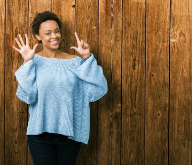 Genç güzel Afrikalı Amerikalı kadın izole arka planda gösteren bir kazak giyiyor ve parmak sayısı yedi ile işaret kadar güven ve mutlu gülümseyen.