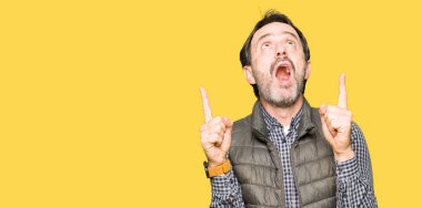 Orta yaş yakışıklı adamın kış yelek giydiğini hayrete ve yukarıya bakıyor ve parmakları ile işaret ve silah kaldırdı şaşırttı.