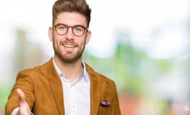 Tebrik ve konuksever dost sunan karşılıklı gülümseyen gözlüklü genç yakışıklı iş adamı. Başarılı iş.