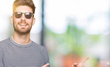 Yakışıklı delikanlı gülümseyen ve iki ile işaret kamera bakarak güneş gözlüğü takıyor eller ve yan parmak.