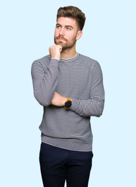 Çene düşünme hakkında soru, dalgın ifade üzerine el ile çizgili süveter giyen genç yakışıklı adam. Düşünceli yüzüyle gülümsüyor. Şüphe kavramı.