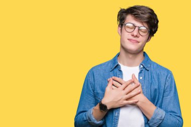 Yakışıklı delikanlı ile gülümseyen izole arka plan üzerinde gözlük takan kapalı gözler ve yüzünde minnettar jest ile göğüs üzerinde eller. Sağlık kavramı.