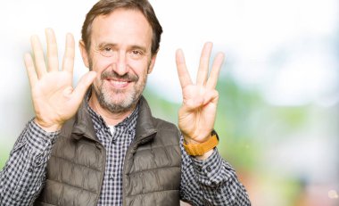 Kış Yelek gösterme ve parmakları ile işaret giyen orta yaş yakışıklı adam kendinden emin ve mutlu gülümseyerek süre sekiz numara.