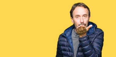 Orta yaş yakışıklı adam öpücük el ile güzel ve seksi olmak yayına üfleme kamera bakarak kış palto giyiyor. Aşk ifade.