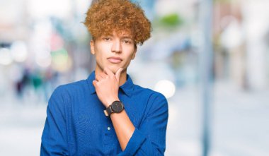 Afro saçlı Genç yakışıklı zarif adam çapraz silah ve el çene üzerinde yükseltilmiş ile gülümseme ile kamera emin görünümlü. Pozitif düşünme.