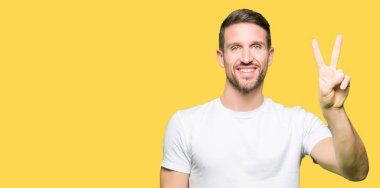 Yakışıklı adam rahat beyaz t-shirt gösteren giyen ve parmak sayısı iki ile işaret kadar güven ve mutlu gülümseyen.