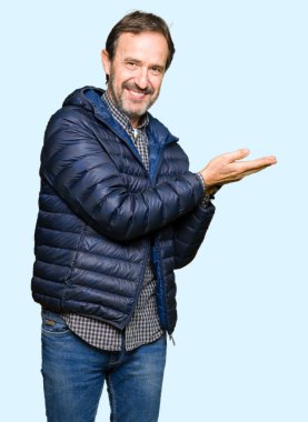 Orta yaş yakışıklı adam giyen kış işaretçi el yanında kat ve açık palm, mutlu ve kendine güvenen reklam gülümseyen sunulması