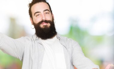 Uzun saç, sakal ve sarılmak için kollarını açarak gülümseyerek kameraya bakarak küpe olan genç adam. Neşeli ifade kucaklayan mutluluk.