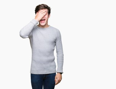 Genç yakışıklı adam gülümsüyor ve gözleri için sürpriz kapsayan yüz el ile gülüyor izole arka plan üzerinde kış kazak giyiyor. Kör kavramı.