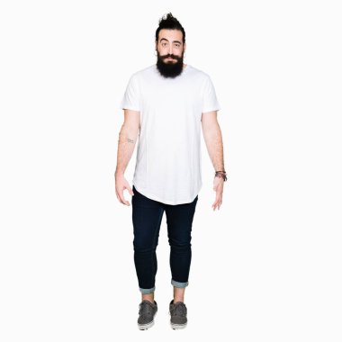 Uzun saç ve sakal komik surat ile rahat beyaz t-shirt şişirme yanakları giyen genç hipster adam. Ağız ile hava, deli ifade şişirilmiş.