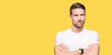 Yakışıklı adam rahat beyaz t-shirt şüpheci ve sinir, kesişmiş kollar ile yüz üzerindeki ifade onaylanmaz giyiyor. Negatif kişi.