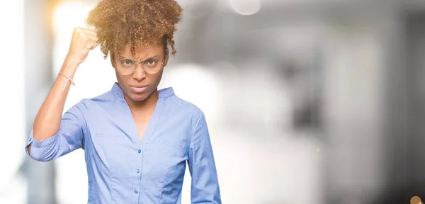 Beautiful young african american business woman over isolated background angry and mad raising fist frustrated and furious while shouting with anger. Rage and aggressive concept.