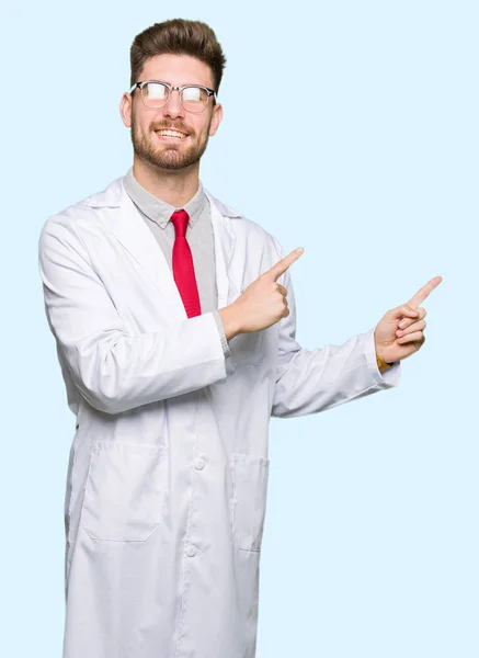 年轻英俊的科学家戴着眼镜微笑着看着镜头 用两只手和手指指着一边 — 图库照片