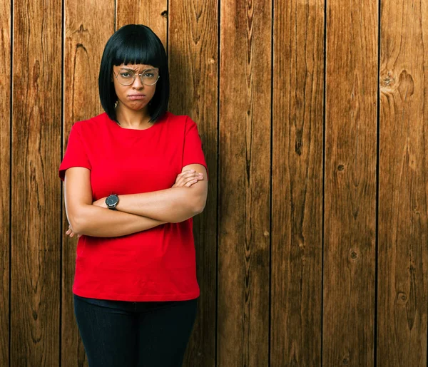 Beautiful young african american woman wearing glasses over isolated background skeptic and nervous, disapproving expression on face with crossed arms. Negative person.
