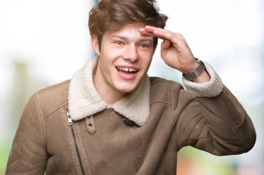 İzole arka plan üzerinde kış ceket giyen genç yakışıklı adam çok mutlu ve gülümsüyor uzağa baş el ile bakıyor. Arama konsepti.