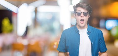 Yakışıklı delikanlı korkuyor ve şok sürpriz ifade, korku ve heyecan yüz ile izole arka plan üzerinde güneş gözlüğü takıyor.