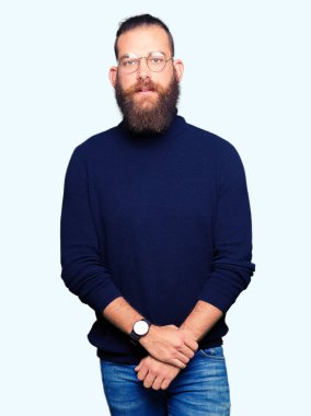 Gözlük ve balıkçı yaka kazak giyen genç sarışın adam birlikte elleri ve çapraz rahat ve neşeli gülümseyen parmak. Başarı ve iyimser