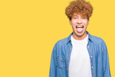 Genç yakışıklı adam ile afro saç giyen denim ceket yapıştırma dil dışarı mutlu ile komik ifade. Duygu konsepti.